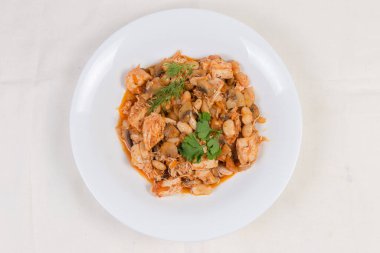 Beyaz masa örtüsünün üzerinde mantarlı fasulye ve domates soslu tavuk porsiyonu.