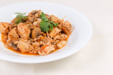 Beyaz masa örtüsünün üzerinde mantarlı güveç fasulyesi ve domates soslu tavuk, yakın plan.