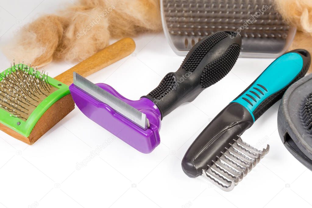 Combs of various purposes for care of pets hair among the brushes and clumps of combed red cat hair close-up
