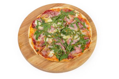 Jambonlu, salamlı ve roka kaplı küçük pişmiş pizza beyaz arka planda yuvarlak ahşap meşe pizza tahtasında kesiliyor.