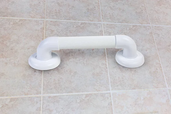 Horizontal white plastic grab bar with grooved handle mounted on bathroom wall with gray tiles, bottom view