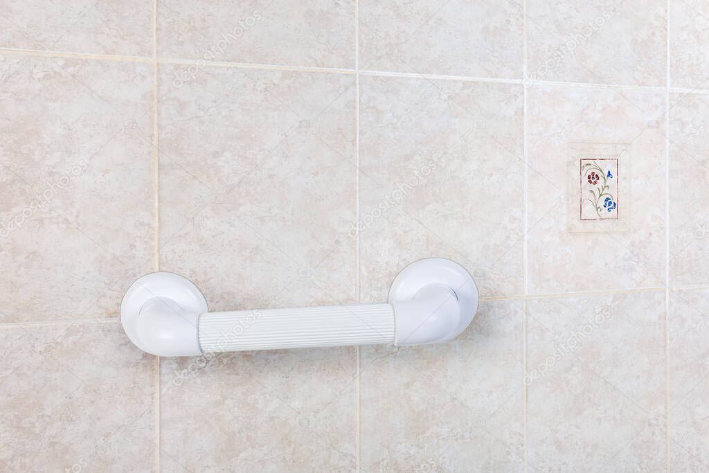 Fragment of the wall with gray tiles in a bathroom with mounted horizontal white plastic grab bar with grooved handle