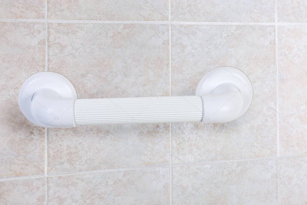 Horizontal white plastic grab bar with grooved handle mounted on bathroom wall with gray tiles, close-up