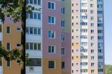 Modern çok katlı apartman kompleksinin ön cephesi. Yazın ön planda dalları olan meşe gövdeli manzarası.