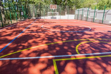 Parktaki ağaçlar arasında çeşitli sporlar yapmak için kırmızı soğurucu kaplama ve renk işaretleriyle evrensel açık hava spor sahası