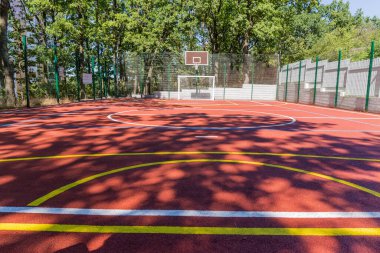Parktaki ağaçlar arasında çeşitli sporlar yapmak için kırmızı emici kaplama ve renk işaretleriyle evrensel açık hava spor alanı, seçici odak noktasında alt görünüm