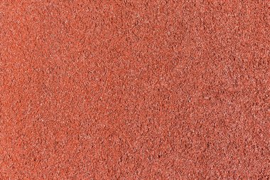 Açık hava spor sahasındaki lastik çiplerden yapılan kırmızı şok emici kaplamanın dokusu, güneş ışığı altında üst görüntü, arka plan.