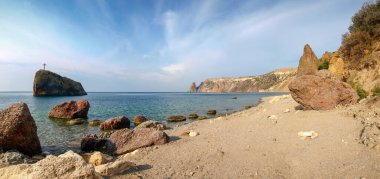 Deniz kıyısında kumlu sahil ve tepesinde kızıl kıyı kayalıkları sabah gökyüzünün arka planında kayalar, panoramik manzara.