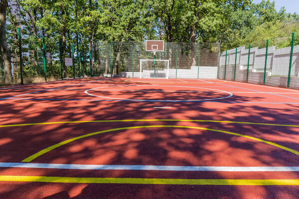 Универсальная открытая спортивная площадка с красно-поглощающим покрытием и цветовой маркировкой для занятий различными видами спорта среди деревьев парка, вид снизу в селективном фокусе