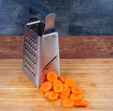 Paslanmaz çelik kutu şeklinde mutfak rendesi ve havuçlar tahta kesme tahtasındaki rende sayesinde daireler şeklinde dilimlenmiş.