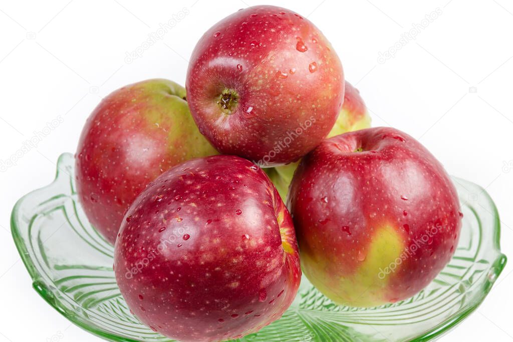 Washed red apples covered with water drops in the green glass dish on a white background, close-up in selective focus