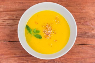 Kabak çorbası püresi, kırmızı mercimek, susam aromalı ve yeşil dallarla süslenmiş eski kırsal masadaki beyaz kase, üst manzara