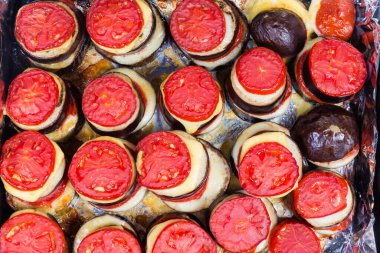 Patlıcanlar daireler şeklinde dilimlenmiş ve fırında domates ve peynirle fırın tepsisinde pişmiş folyoyla kaplı.