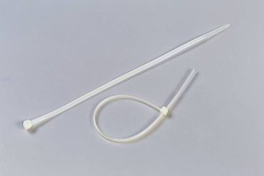 One unfastened and one fastened single-use nylon white translucent cable ties a gray background clipart