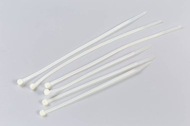 Several unfastened single-use nylon white translucent cable ties of different lengths on a gray background clipart