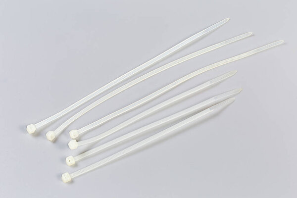 Several unfastened single-use nylon white translucent cable ties of different lengths on a gray background