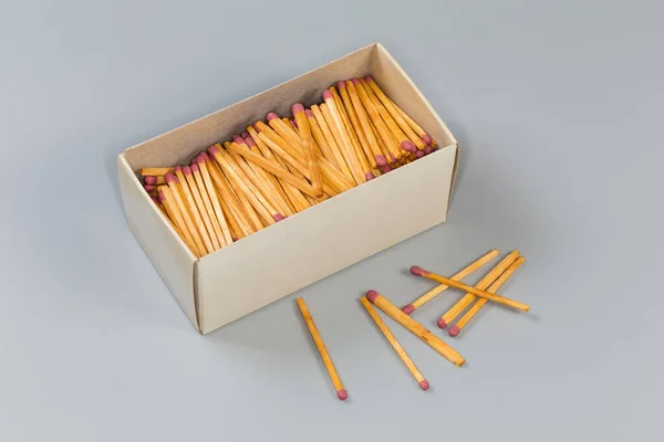 Wooden household safety matches in open large cardboard matchbox and several the same matches beside on a gray surface