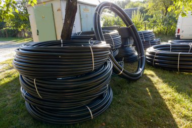 Farklı çaplarda siyah yuvarlak plastik borulardan oluşan büyük bobinler. Güneşli bir gecede açık havada çimlerin üzerine yığılmış belediye doğalgaz boru hattı inşaatı için sarı işaretli borular.