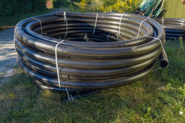 Belediye doğalgaz boru hattı inşaatı için sarı işaretli büyük siyah yuvarlak plastik boru bobini güneşli bir akşamda çimlerin üzerinde uzanır.