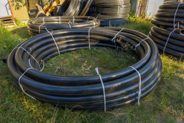 Şehir doğalgaz boru hattı inşaatı için sarı işaretli farklı çaplı siyah yuvarlak plastik borular güneşli bir akşamda açık havada uzanır.