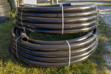 Belediye doğalgaz boru hattı inşaatı için sarı işaretli siyah yuvarlak plastik boru bobinleri güneşli akşamlarda açık havada uzanır.