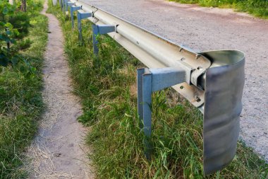 Zincirli çelikten yapılma çarpışmaya dayanıklı yol kazası bariyerinin sonu, toprak yol kenarına monte edilmiş, yol kenarından seçici bir odak noktasıyla yakın çekim.