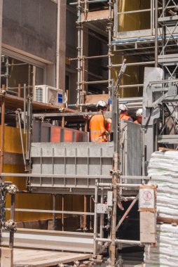 Bir şantiye turuncu ceket ve kask ile üç işçi ile görünümünü