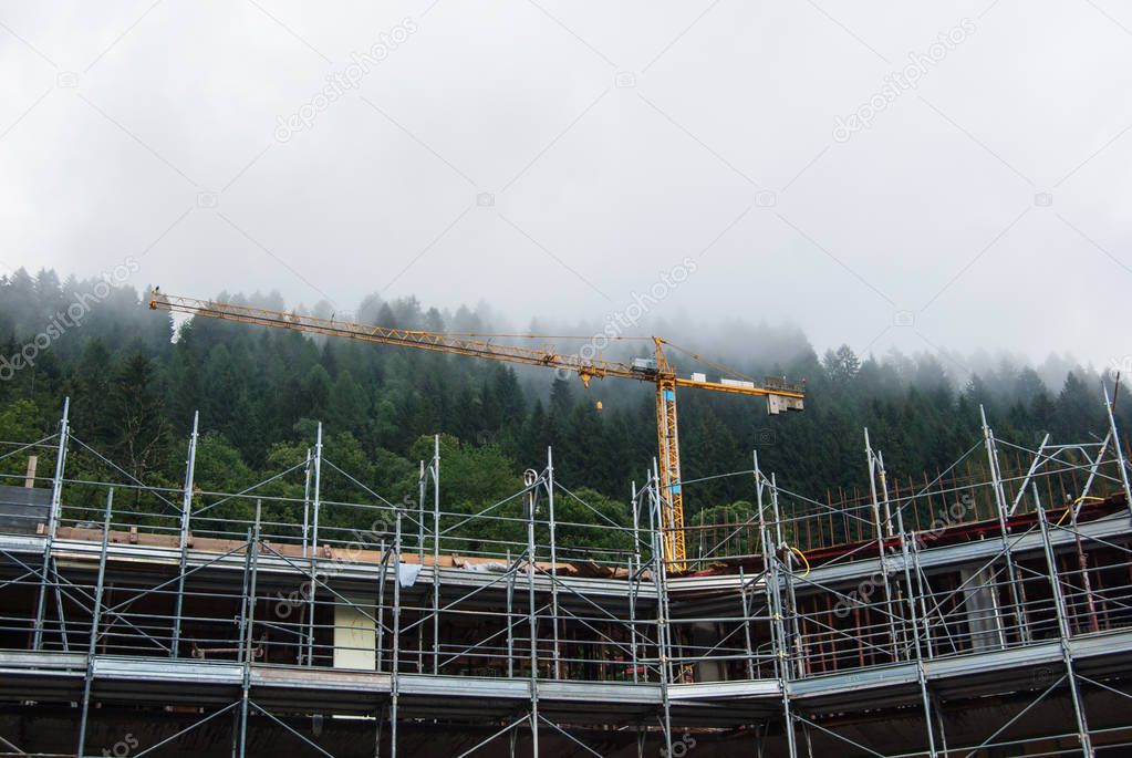 Metal scaffolding and yellow cranes with low clouds above the Abies of a forest