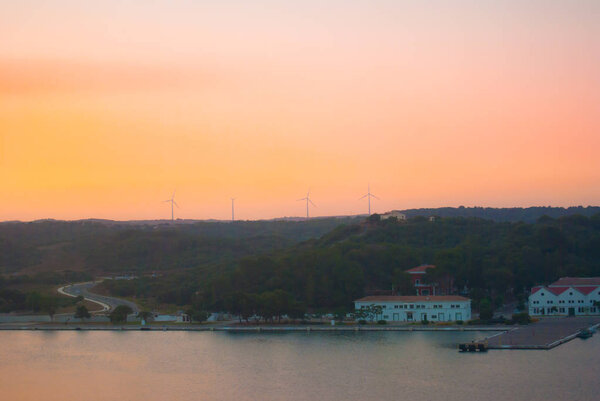 Four wind turbines during the sunset on Mahon harbor and reflection on the sea