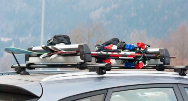 Arabanın çatısında iki çift kayak ve bir snowboard.