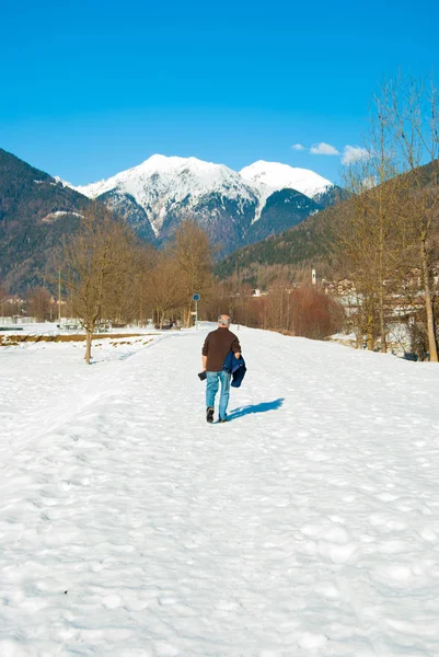 老人在阳光明媚 温暖的日子里 带着山的全景走在雪中 — 图库照片