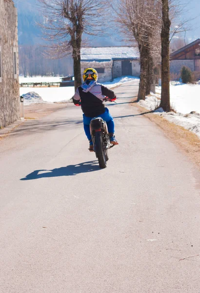 Single man on motocross on a road with snow and bare trees