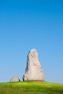 Temiz ve mavi gökyüzü ile yeşil çimenlerin üzerinde yan yana iki gri dikilitaş