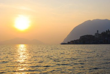 Houses of Monte Isola island and reflection of the sun on the water of the Iseo lake clipart