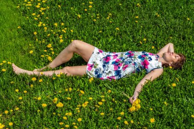 Karahindiba ile yeşil çimenlerin üzerinde bir pamuk içinde bir kadın yatıyor