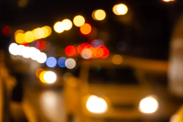 The abstract beautiful blurred background with a group of multi colored blue, white, red circles from street lights and blurry white car lights and a blurred white car at night on a road