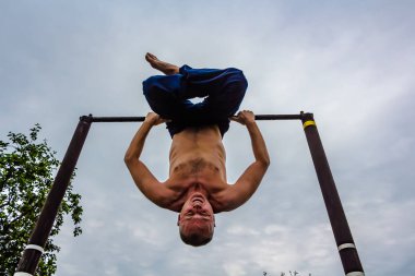Bir adam baş aşağı yatay bir çubuk üzerinde onun sabah egzersizleri yapıyor mavi pantolon içinde çıplak bir gövde ile