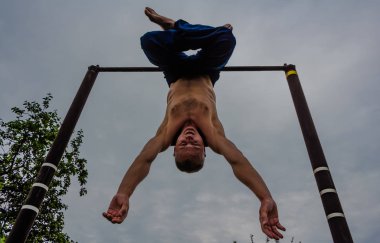 Bir adam baş aşağı yatay bir çubuk üzerinde onun sabah egzersizleri yapıyor mavi pantolon içinde çıplak bir gövde ile