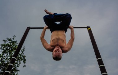 Bir adam baş aşağı yatay bir çubuk üzerinde onun sabah egzersizleri yapıyor mavi pantolon içinde çıplak bir gövde ile