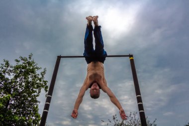 Bir adam baş aşağı yatay bir çubuk üzerinde onun sabah egzersizleri yapıyor mavi pantolon içinde çıplak bir gövde ile