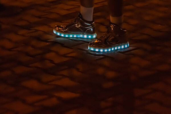 The luminous shoes are on legs on the dark background