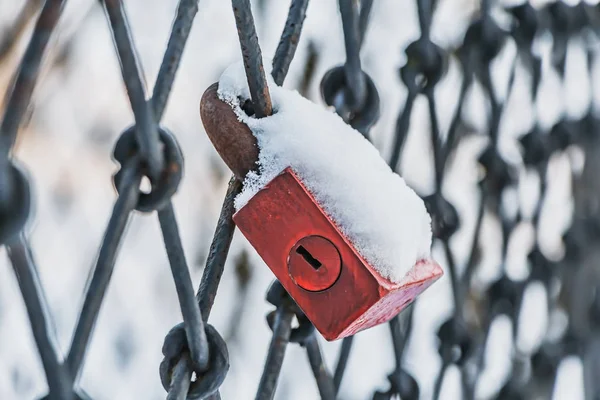 雪の公園で黒い金属の鉄格子にハングアップする白い雪と古い赤い色ロック — ストック写真