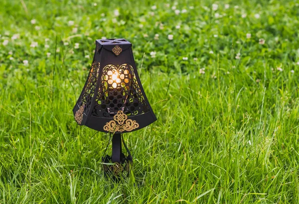 Piękne czarne ażurowe metalowe lampy retro z złoty ornament i żółte światło pali na tle zielonej trawie — Zdjęcie stockowe