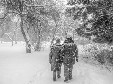 Bir siyah beyaz yatay yaşlı retro fotoğraf iki yaşlı adamın kışın karlı bir parkta bir yol boyunca yürüme