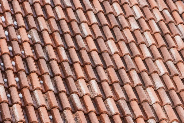 A beautiful horizontal texture of part of an old wet brown roof of clay tiles with white snow is in winter