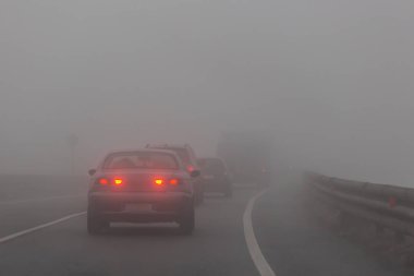 A group of cars with red lights is on the road in the fog clipart