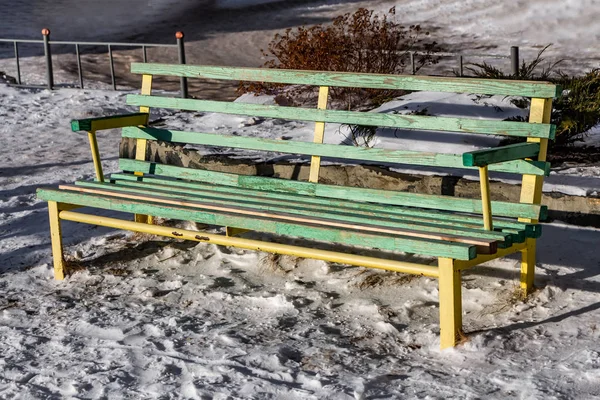 一个明亮的湿木漆成黄色和绿色美丽的长凳与黄色的金属腿站在白雪在院子里的冬天 — 图库照片