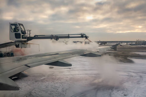 在冬季日出的时候 在机场 在飞机机翼的后部喷洒防冰白液的过程是在蓝色的天空上 有粉红色的云 — 图库照片