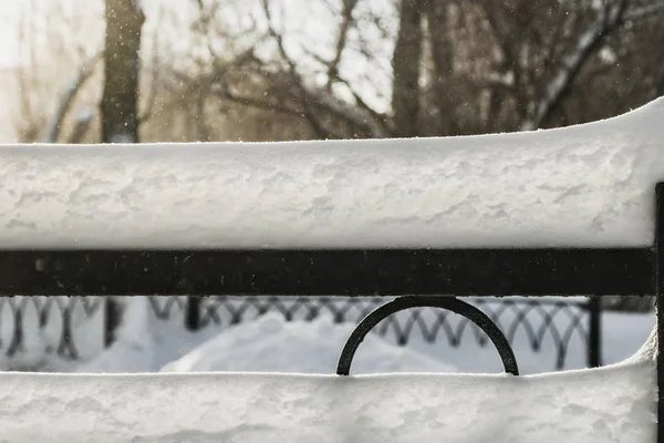 Eine Schneewehe aus weißem Schnee mit Sonnenschein und Bokeh-Licht auf einem schwarzen, aus Metall geschmiedeten Zaun vor verschwommenem Hintergrund in einem Park im Winter — Stockfoto