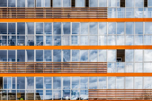 Un nuevo edificio moderno de dormitorio de estudiantes en el campus con muchas ventanas con reflejos de cielo azul con nubes blancas. Textura horisontal de ventanas azules y decoración naranja — Foto de Stock